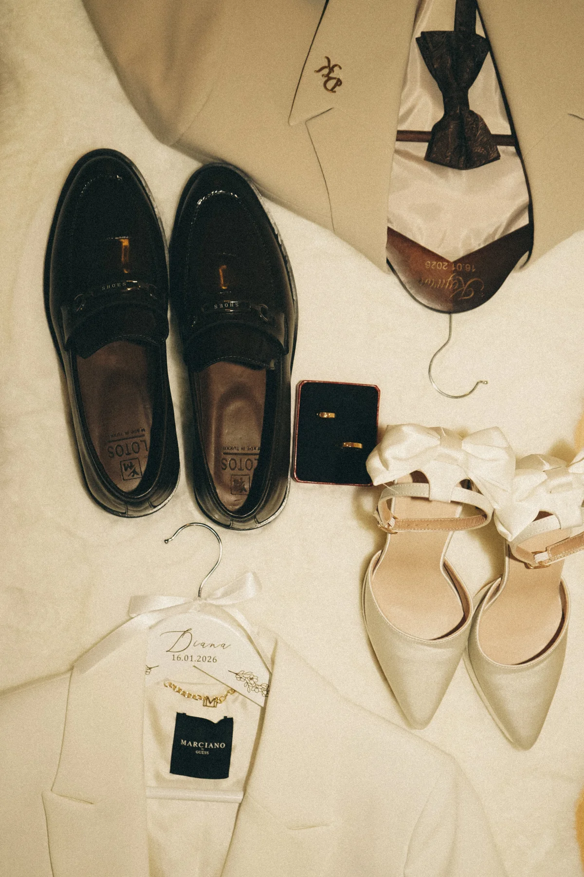 Schwarze Lederschuhe, helle Pumps, ein Ringetui und ein heller Anzug mit schwarzer Fliege.